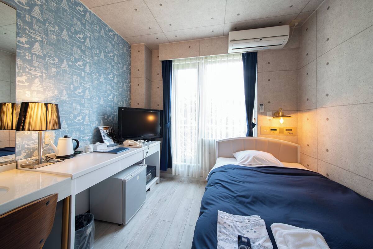 Habitación de hotel con cama, escritorio, televisor y ventana con cortinas.