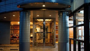 A hotel entrance with a revolving door, tiled columns, and a well-lit interior visible through the glass doors. - Asuka Hotel (Karatsu)