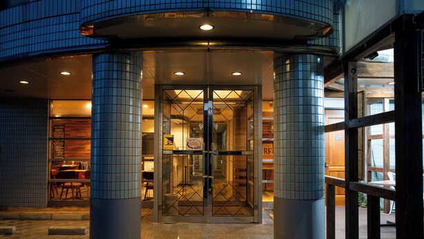 Una entrada de hotel con puerta giratoria, columnas de azulejos y un interior bien iluminado visible a través de los cristales.