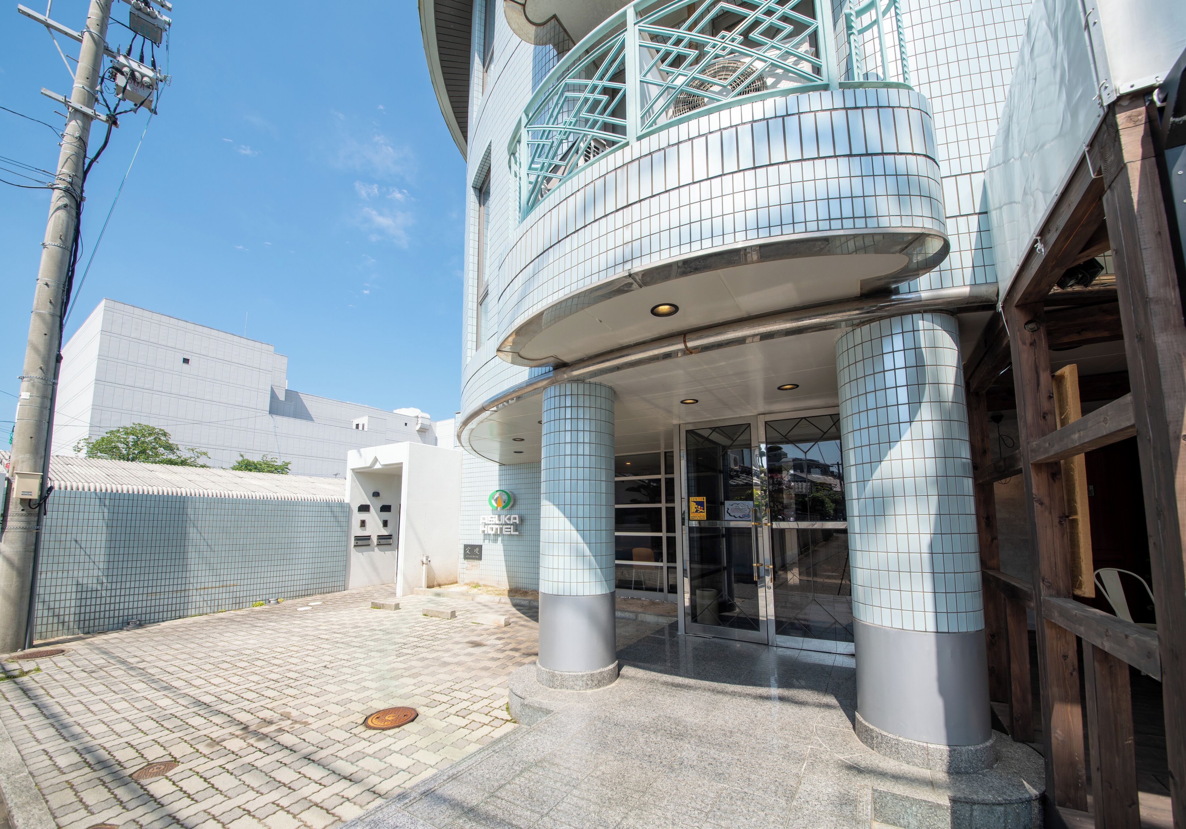 A hotel entrance with a tiled facade, a balcony with blue railings, and a clear sky.