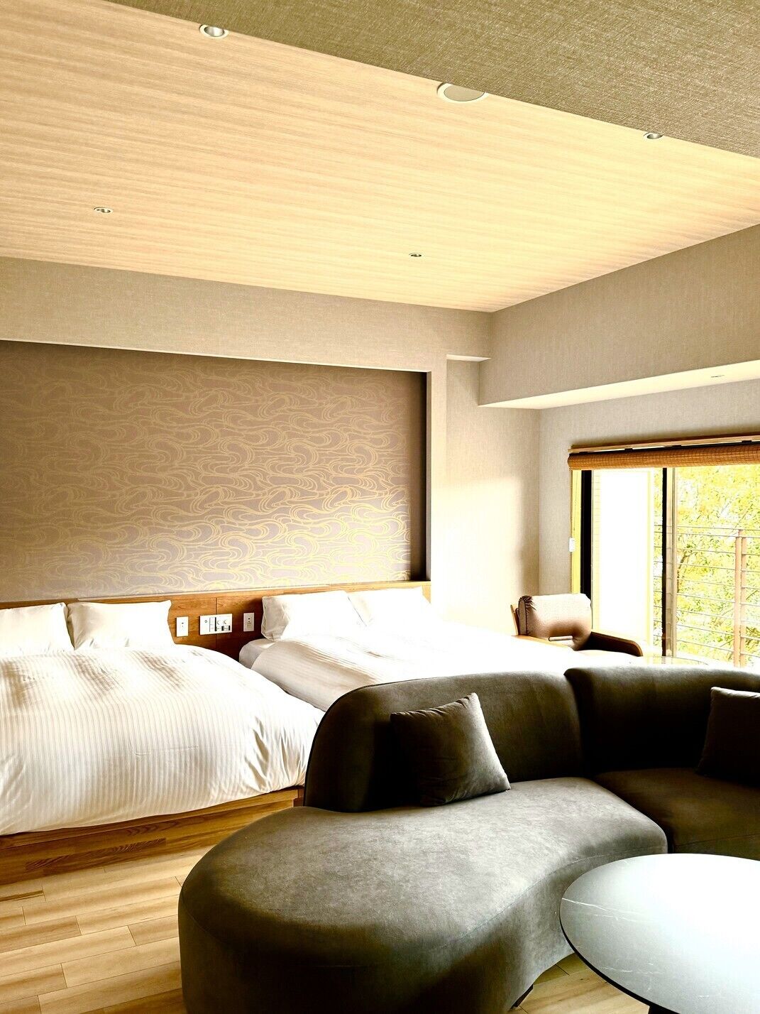 A modern hotel room with a large bed, a sofa, and a window with a view.