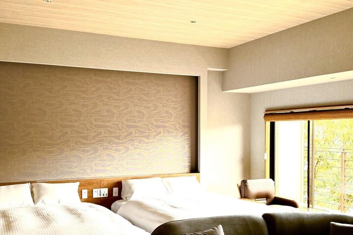 A modern hotel room with a large bed, a sofa, and a window with a view.