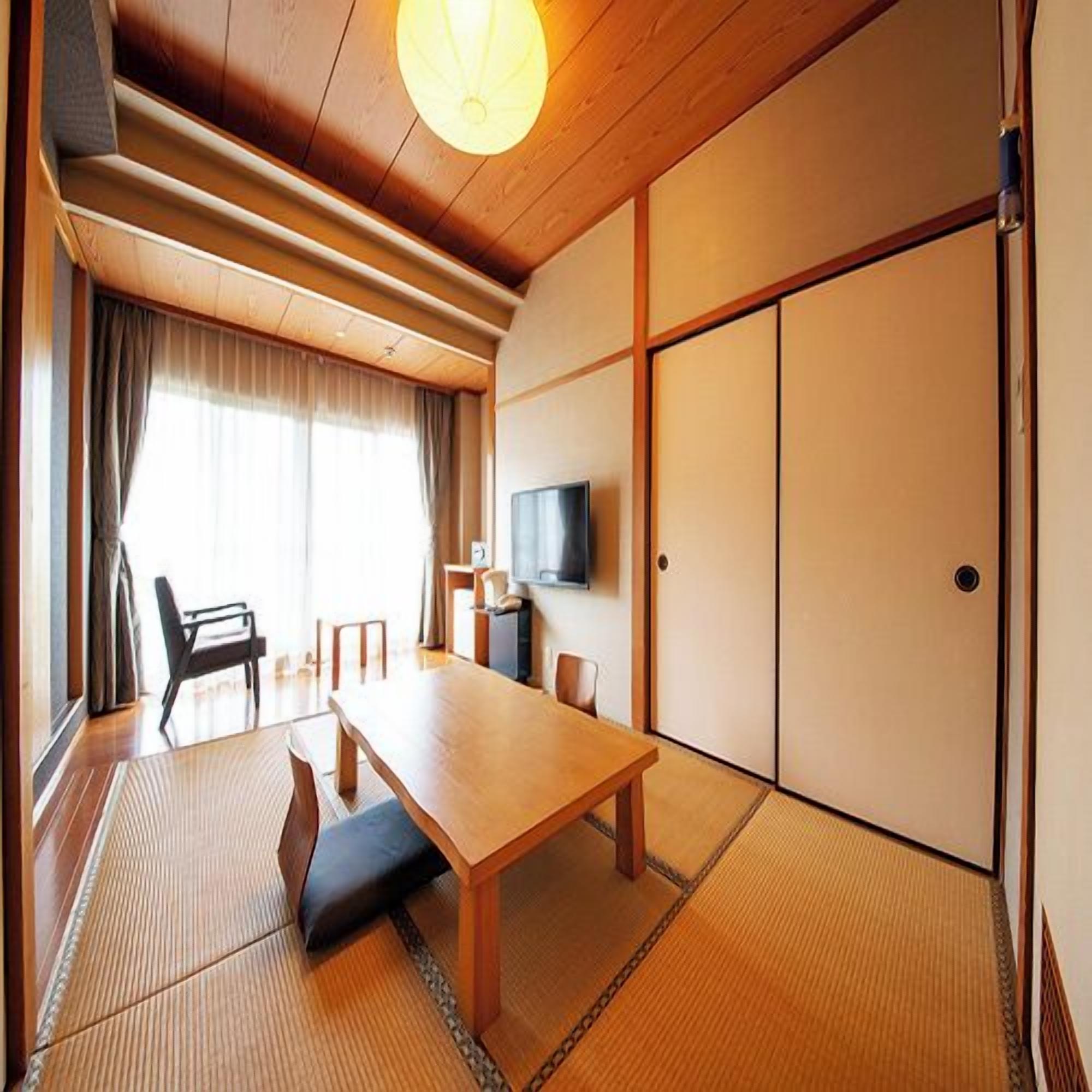 Um quarto japonês tradicional com tatames, uma mesa baixa, uma televisão e portas de correr.