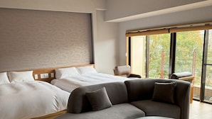A modern hotel room with a large bed, a sofa, a round table, and a view of trees through large windows. - Hana No Shizuku (Ureshino)