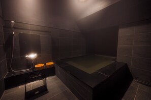 A modern bathroom with a large bathtub, two wooden bowls, and a handheld showerhead.