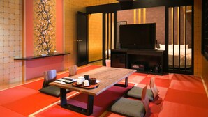 A modern hotel room with a wooden dining table, red tatami mats, a television, and a sliding door leading to a bed. - Hana No Shizuku (Ureshino)