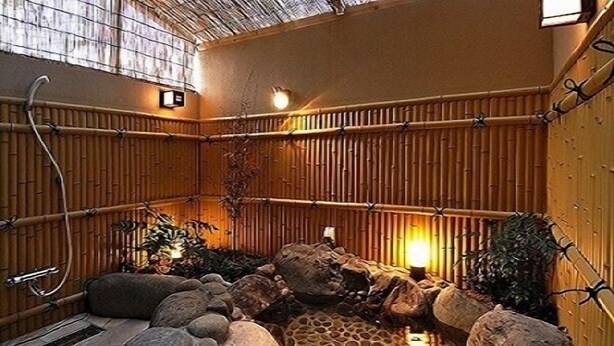 A traditional Japanese onsen with a stone hot spring, bamboo walls, and a tiled floor. - Hana No Shizuku (Ureshino)
