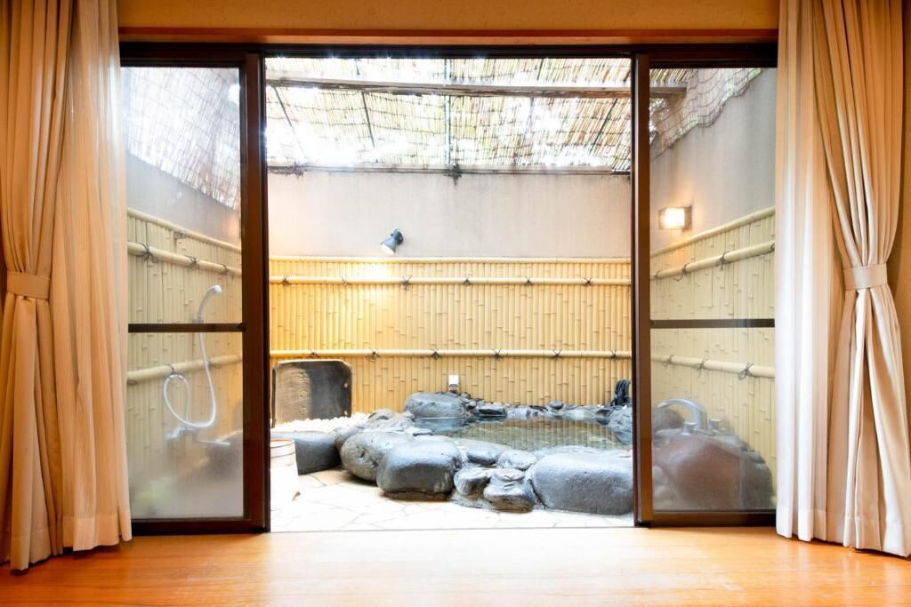 A traditional Japanese room with tatami flooring, a shoji screen door, and a view of an outdoor garden with a hot spring.