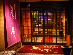 A traditional Japanese entrance with a sliding door, a red carpet with gold writing, and a stone lantern.