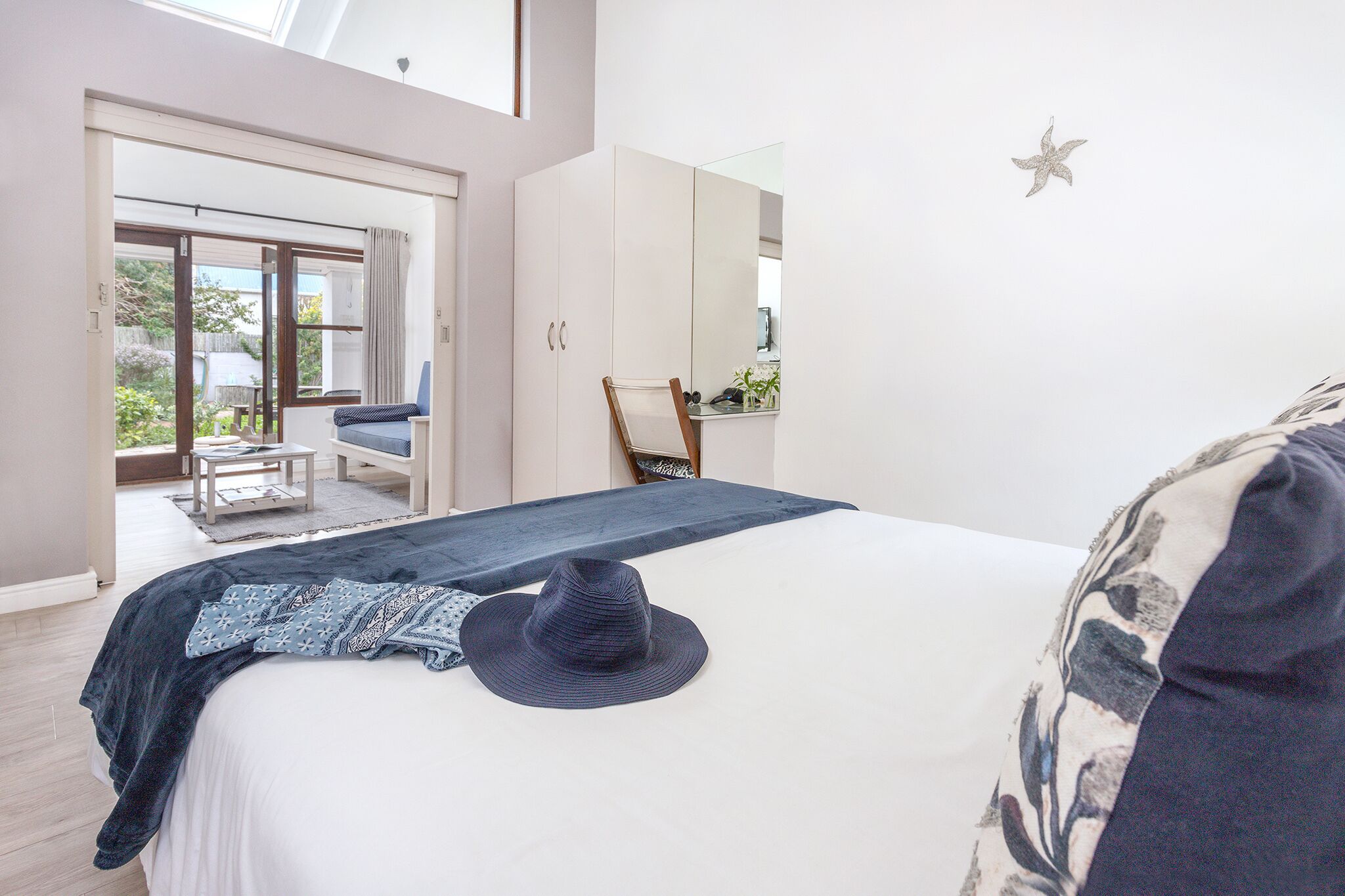 Une chambre à coucher avec un grand lit, une table de chevet, une commode et une fenêtre donnant sur l’extérieur.
