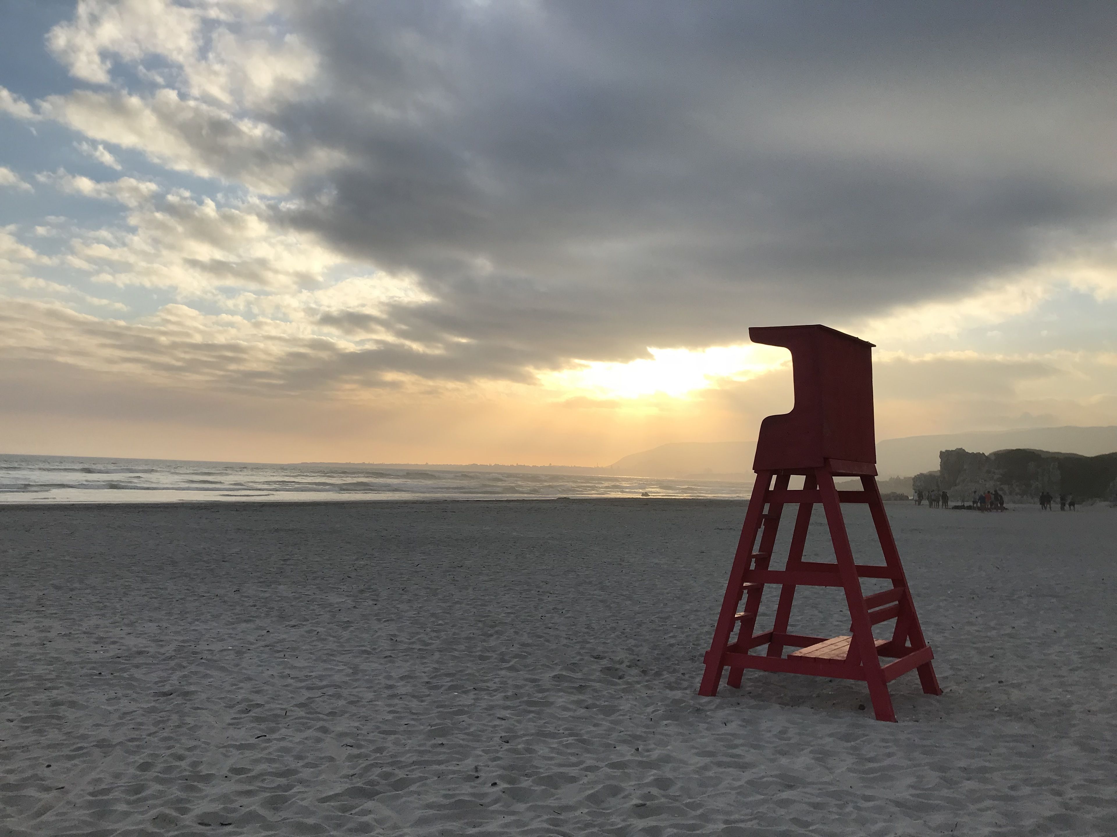 Uma torre de salva-vidas numa praia, com o oceano e um céu nublado ao fundo.