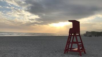 Uma torre de salva-vidas numa praia, com o oceano e um céu nublado ao fundo.
