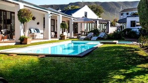 Et moderne hus med swimmingpool, udendørs møbler og udsigt til bjerge.