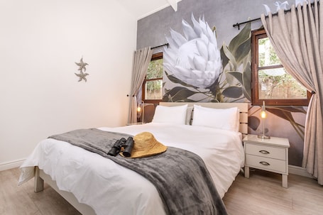 A bedroom with a large bed, a nightstand, a lamp, and a window with curtains.