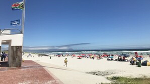 En strand med et flagstang, badegæster og parasoller.