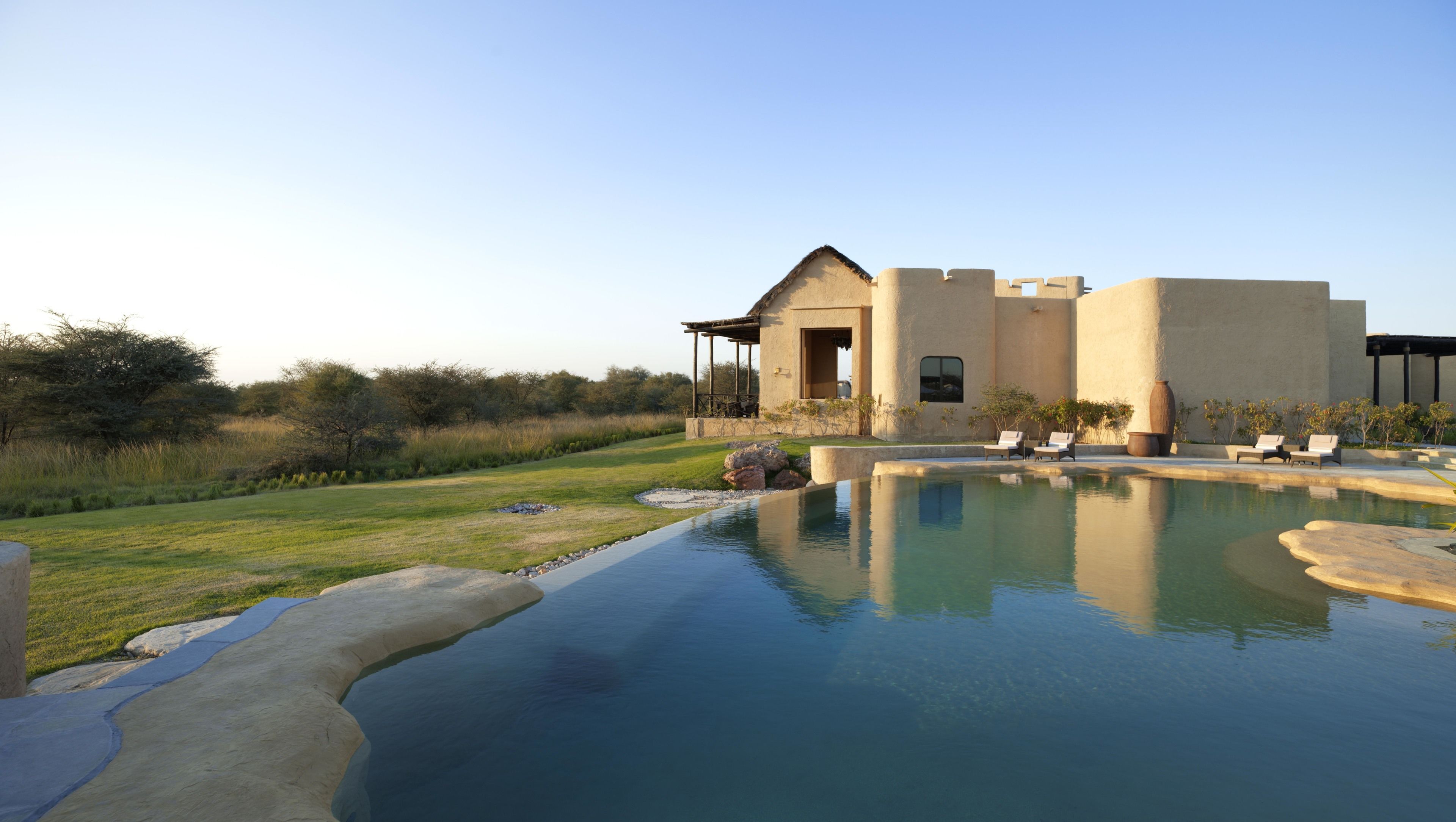 A modern house with a swimming pool, outdoor seating, and a well-maintained lawn.