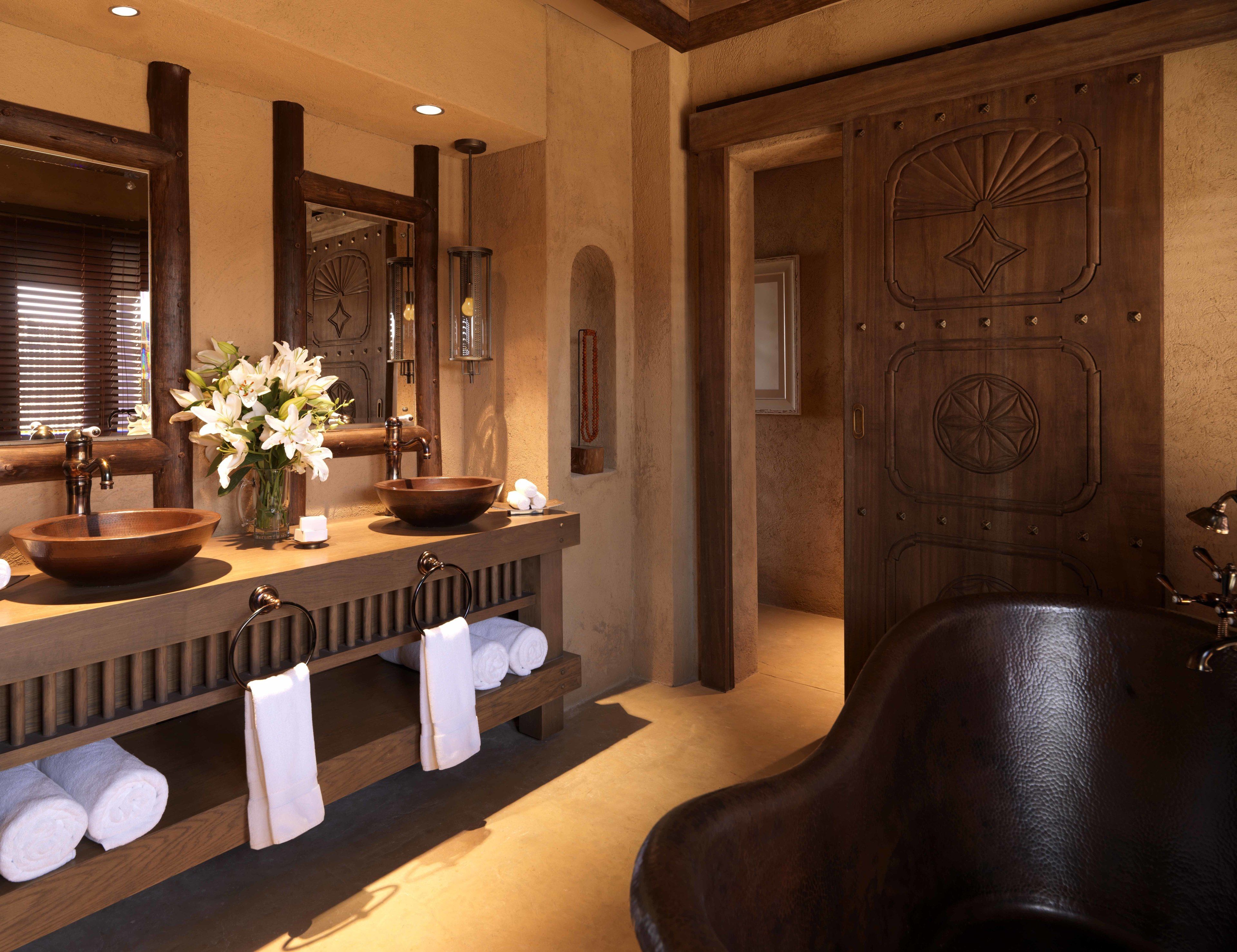 A bathroom with a wooden vanity, a large mirror, a bowl sink, a freestanding bathtub, and towels on shelves.
