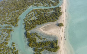 An aerial view of a coastal area with a sandy beach, clear turquoise waters, and dense green vegetation.