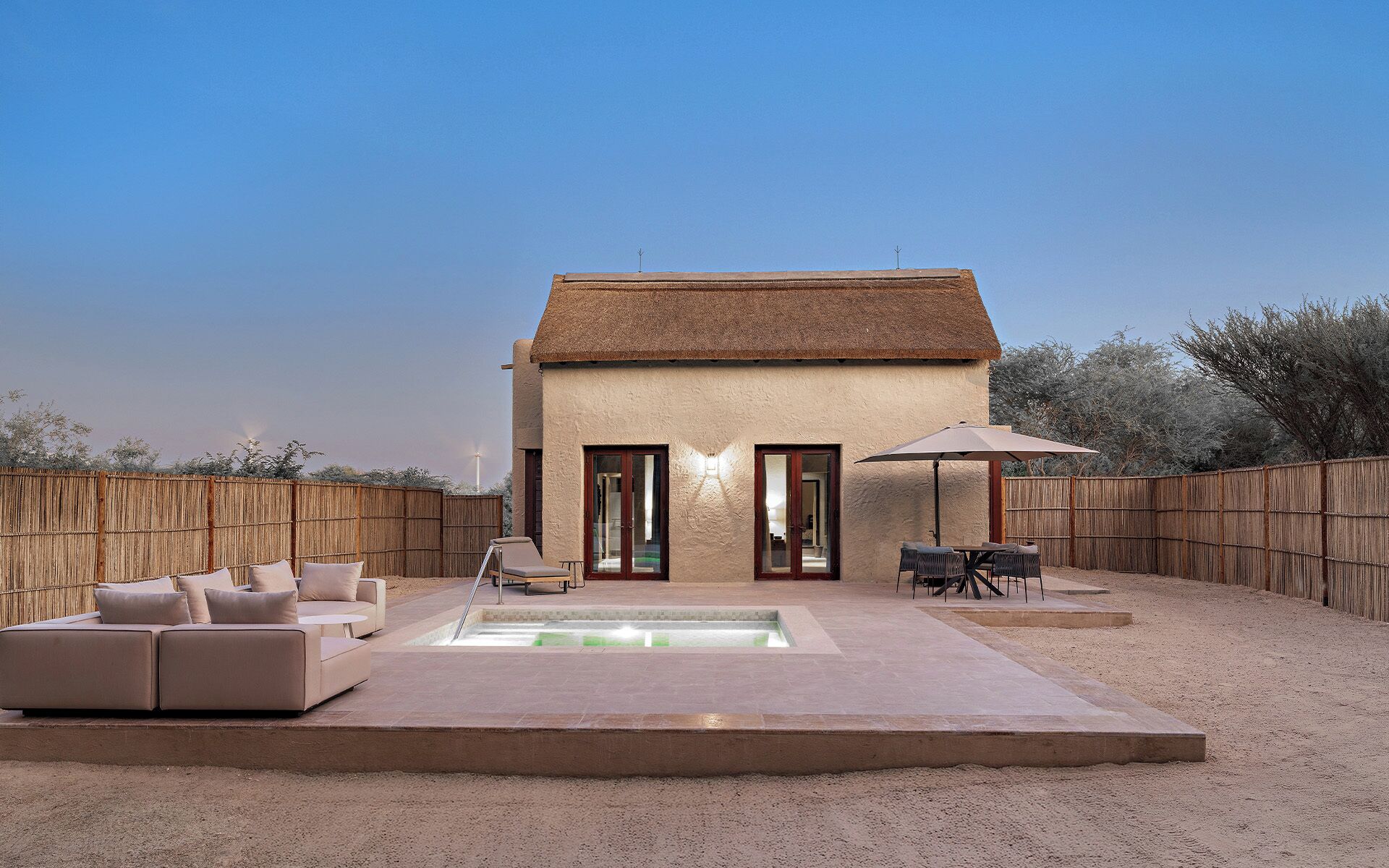 A house with a thatched roof, a swimming pool, and a fenced backyard with outdoor furniture.