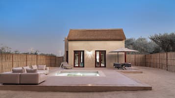 A house with a thatched roof, a swimming pool, and a fenced backyard with outdoor furniture.