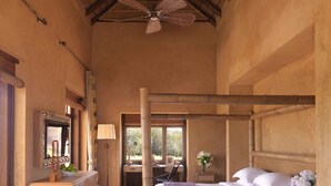 A spacious bedroom with a large bed, a wooden desk, a chair, a vanity with a mirror, and a ceiling fan.