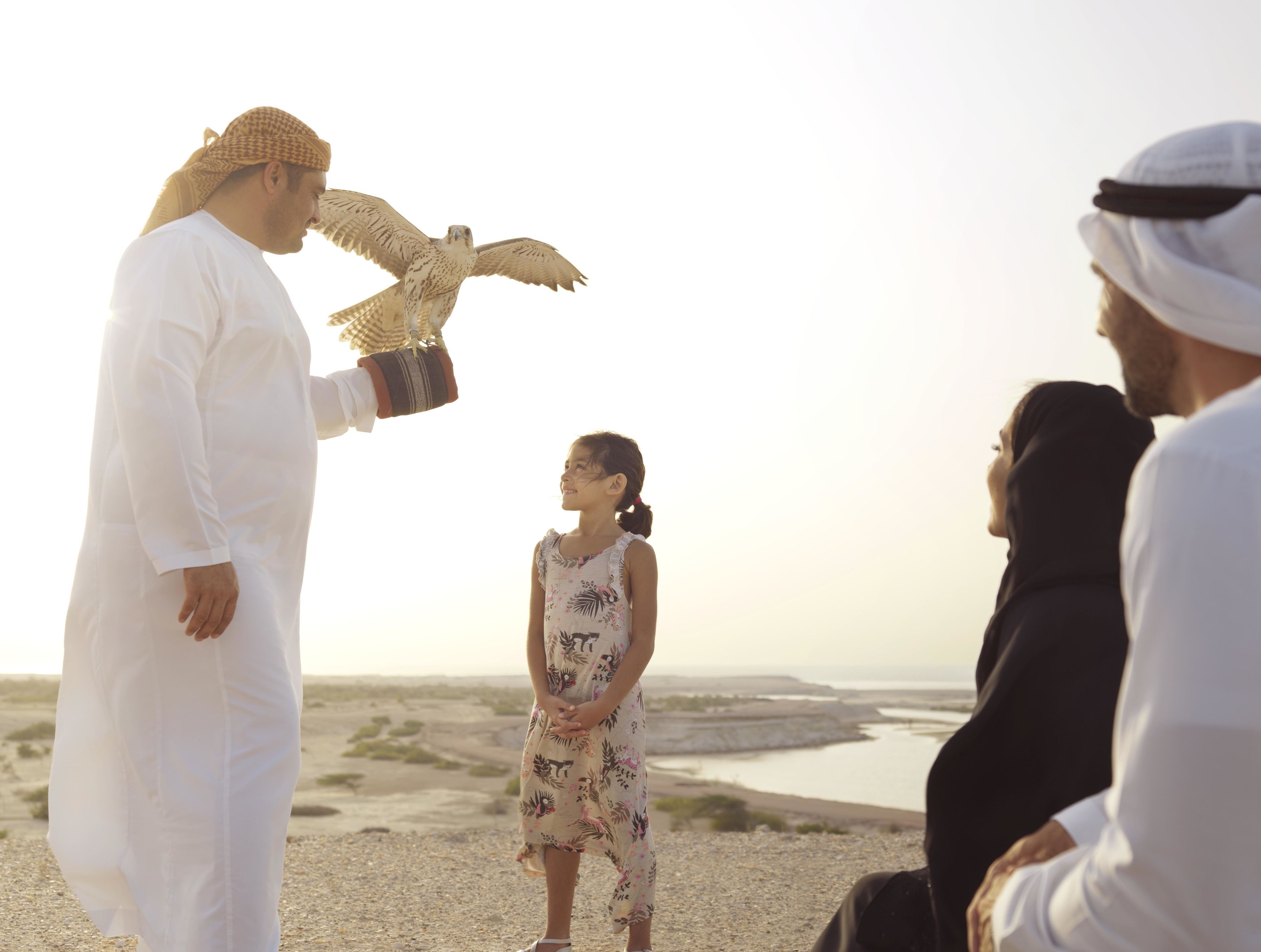 A group of people on a beach with a falcon flying above.