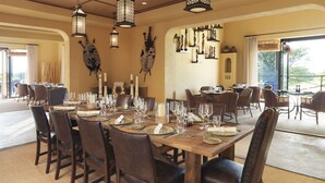 A dining area with a large wooden table set for a meal, surrounded by wicker chairs.