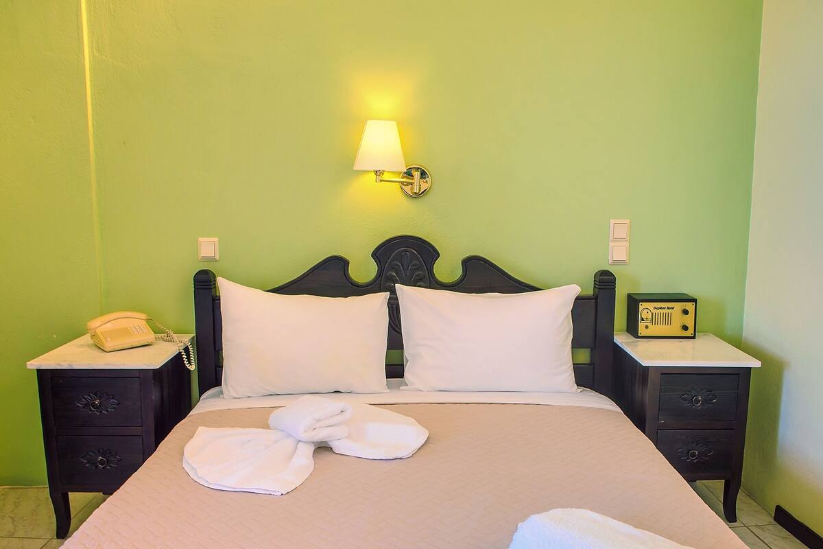 A neatly made bed with white pillows and towels, a bedside lamp, a telephone, and a small table with a clock and a sign that reads "Dolphin Hotel".