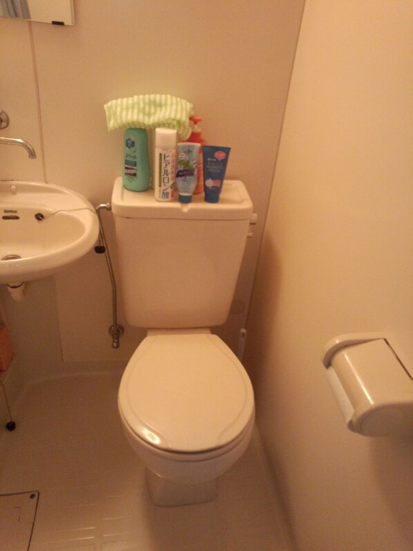 Une salle de bain équipée de toilettes, d’un lavabo et de produits de toilette placés sur le réservoir des toilettes.