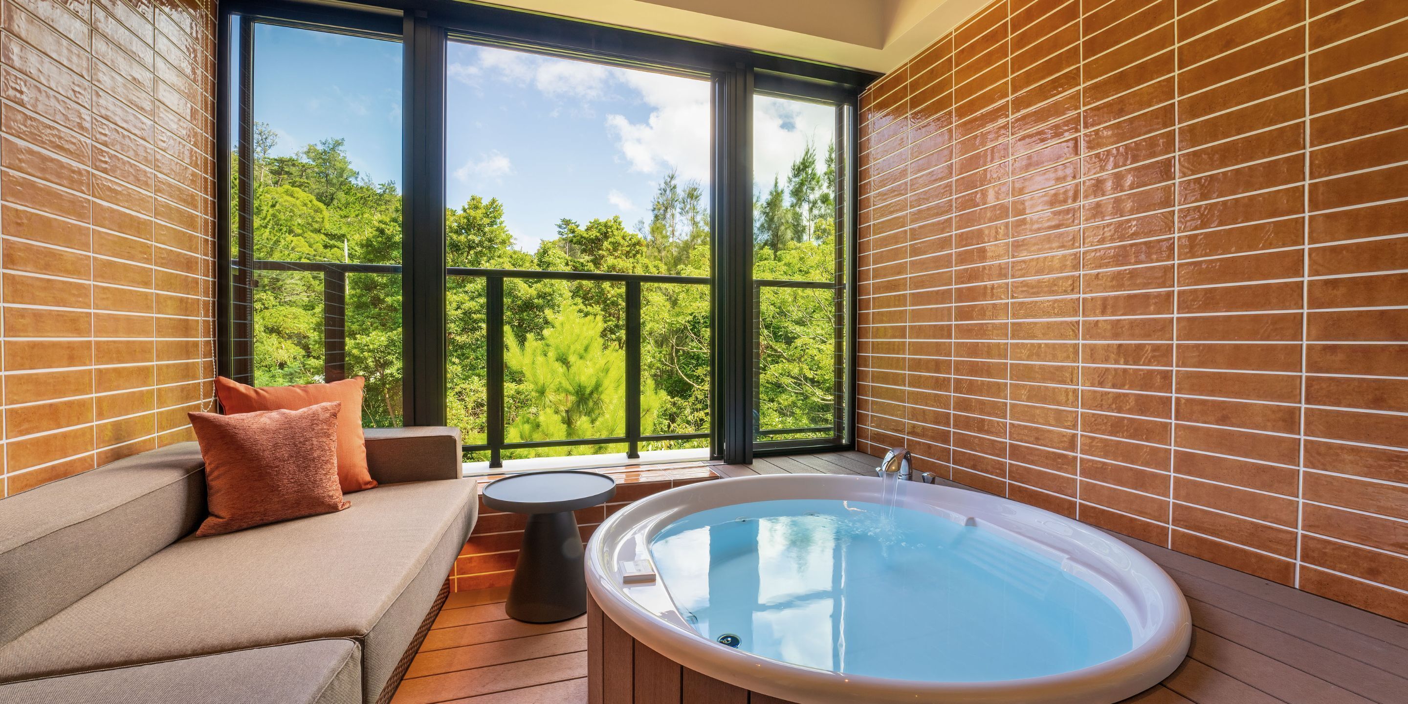 A modern bathroom with a large window, a bathtub, a sofa, and a small table.