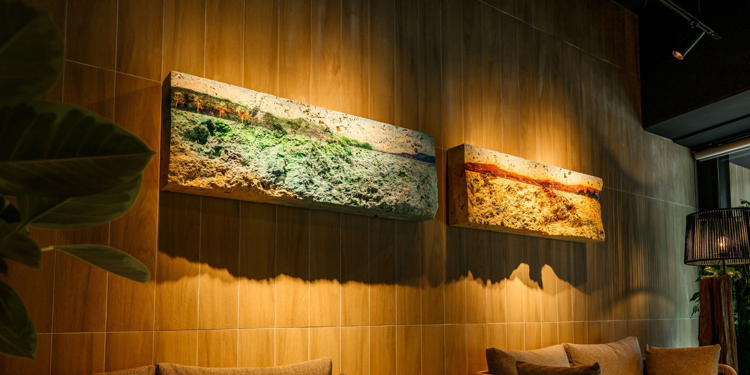 A room with wooden panel walls, two large textured wall art pieces, and a modern lamp.