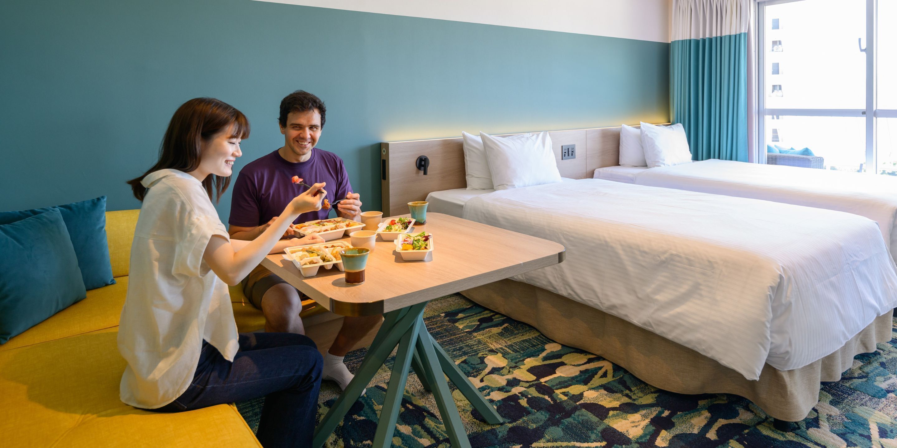 A hotel room with two beds, a small dining table with food, and a sofa.