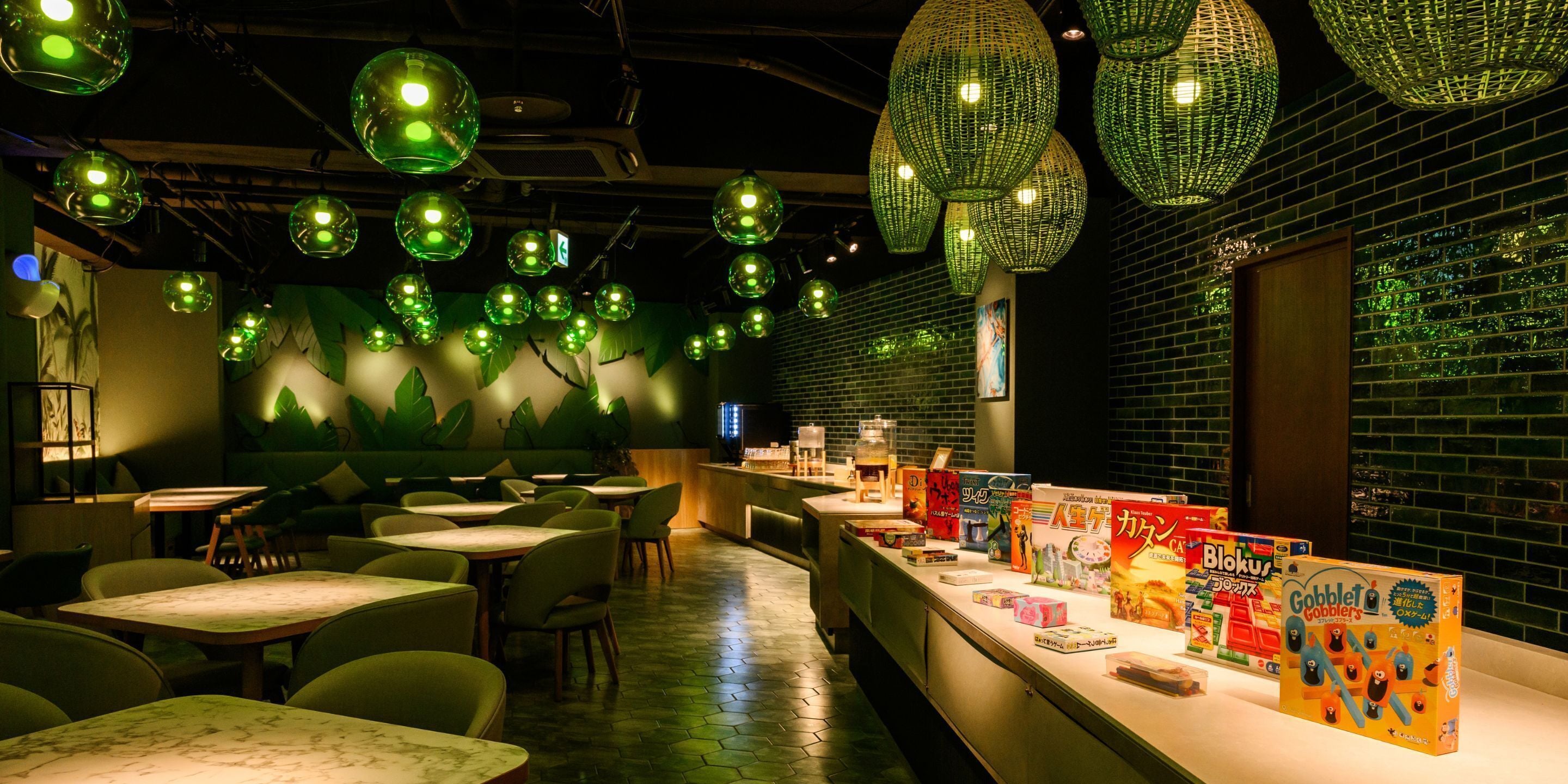 A restaurant with a long counter, green hanging lights, and a brick wall.