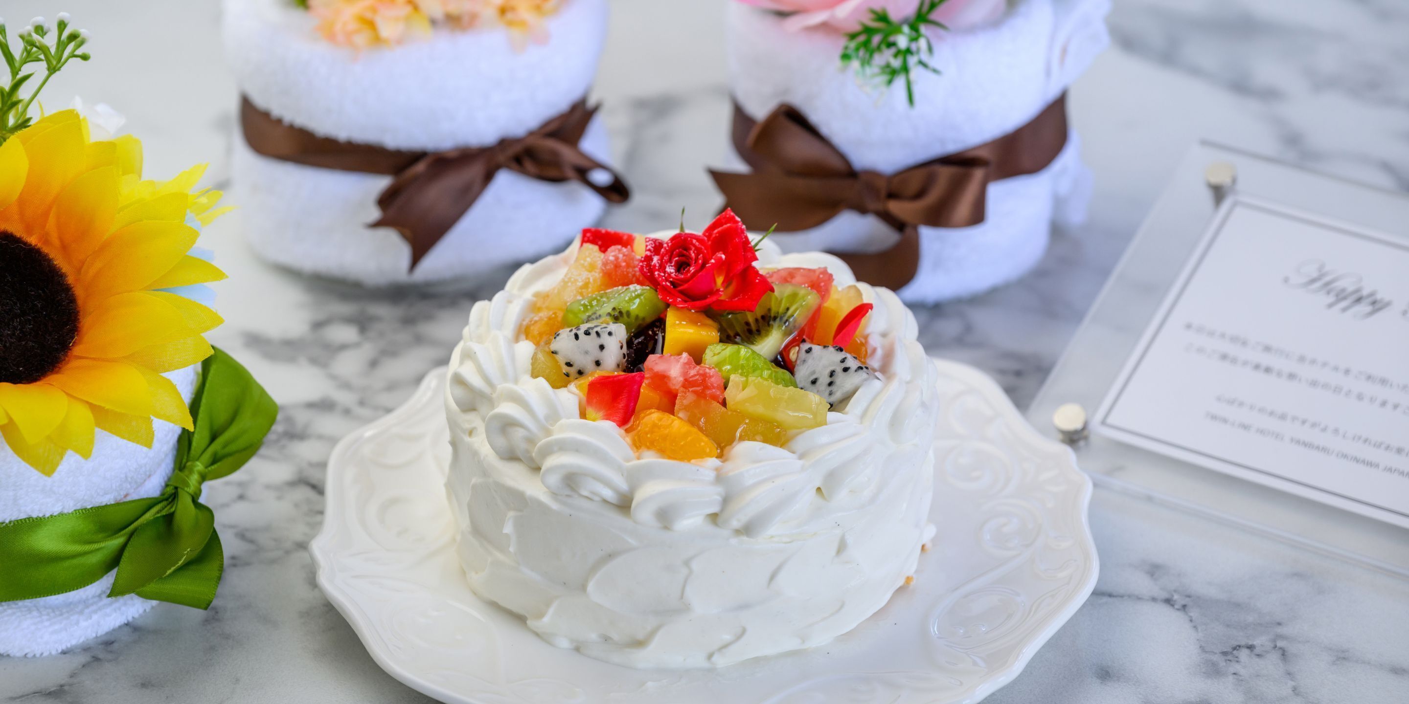 Un postre con crema batida y fruta, una girasol y una invitación de boda sobre una mesa de mármol.