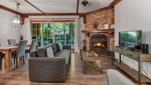 A living room with a stone fireplace, a television, and a dining area with a wooden table and chairs.