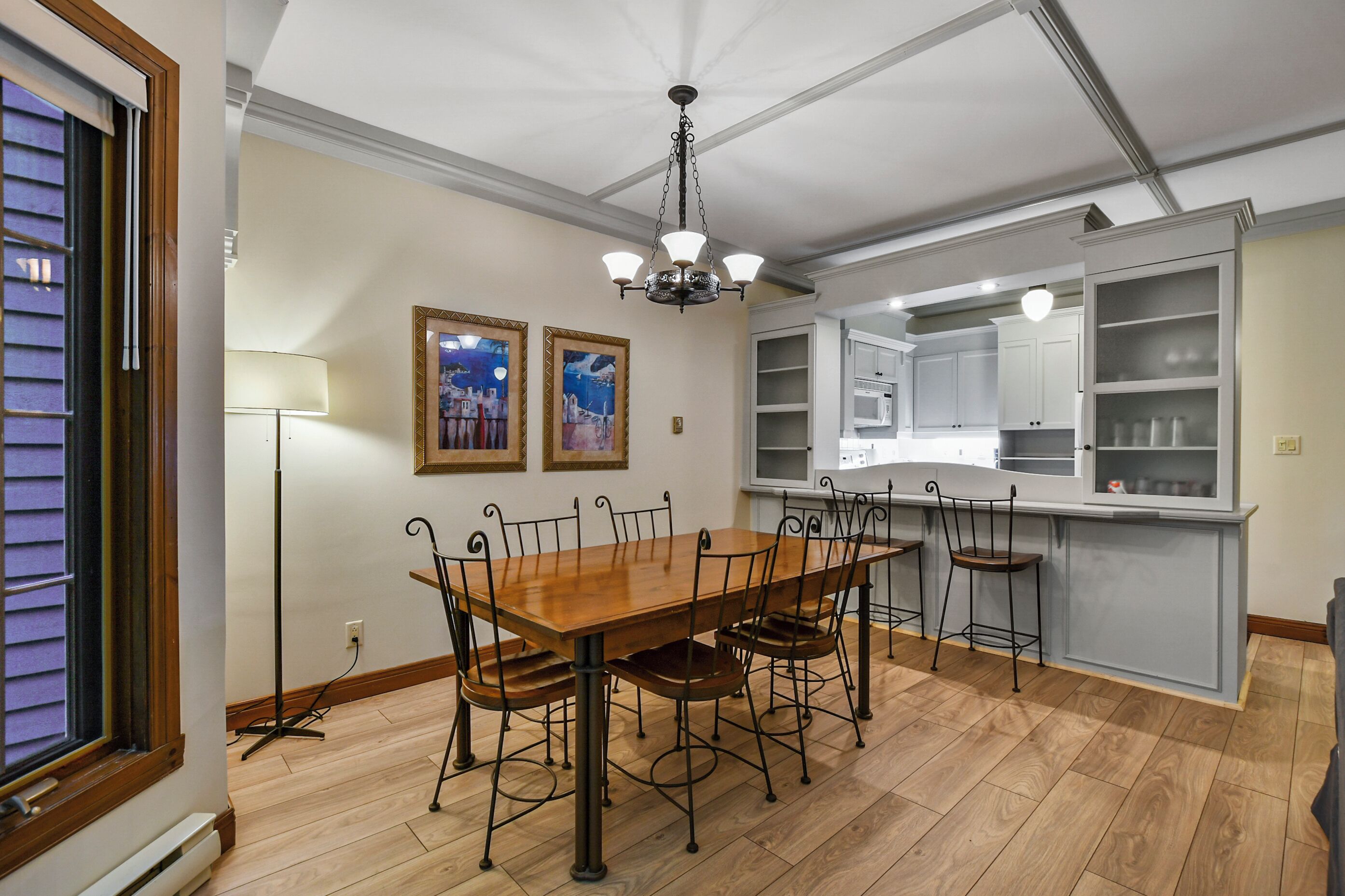 Un comedor con una mesa y sillas de madera, un candelabro, y una cocina con armarios blancos.