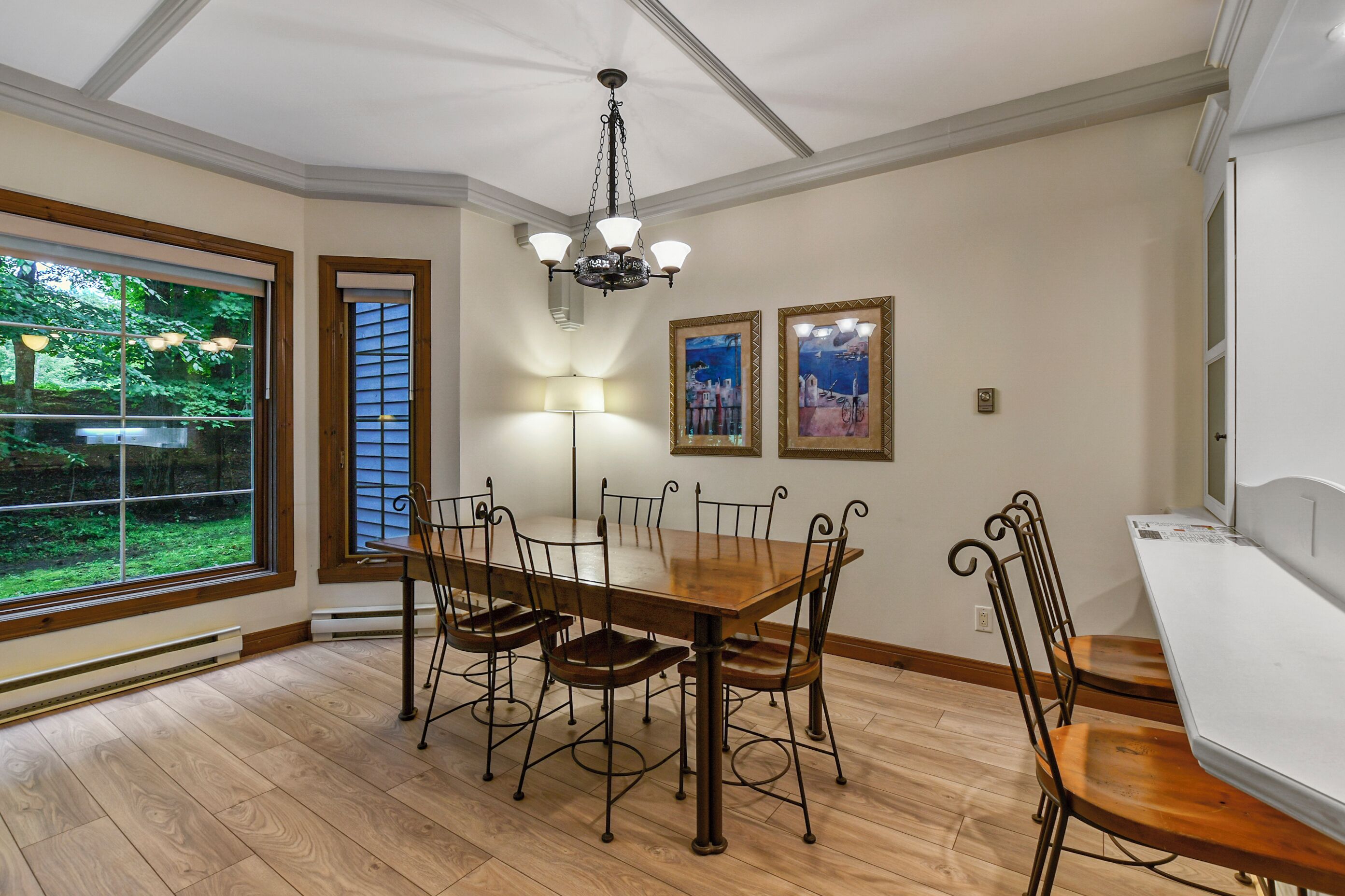A dining room with a wooden table and chairs, a chandelier, and framed artwork on the wall.