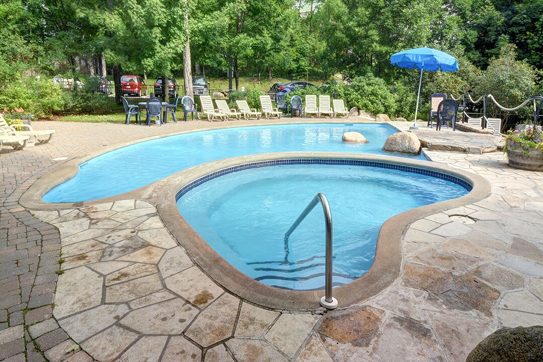 Una piscina con plataforma de piedra, sillas de descanso y un paraguas azul.