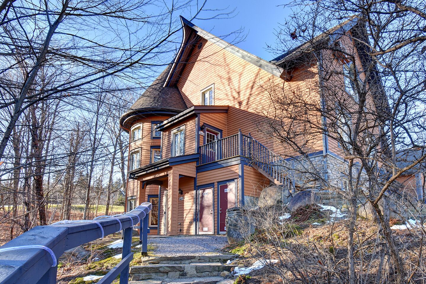 Ein zweistöckiges Haus mit einem steilen Satteldach, einem Balkon im zweiten Stock und einer Steintreppe, die zum Eingang führt.