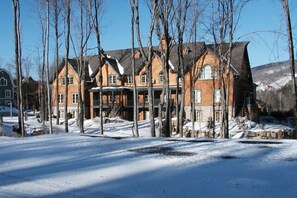 A large, multi-story building with a symmetrical facade, multiple windows, and a prominent entrance with steps. - Les Manoirs - RVMT (Mont-Tremblant)