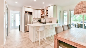 A modern kitchen with a central island, white bar stools, and a wooden dining table. - L'Aiglon - RVMT (Mont-Tremblant)