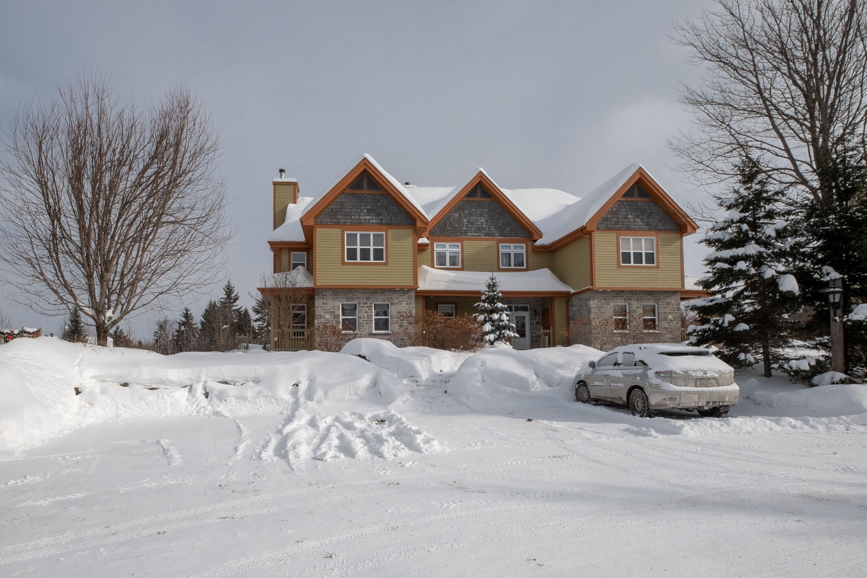 A large, multi-story house with a stone facade and a snow-covered roof.