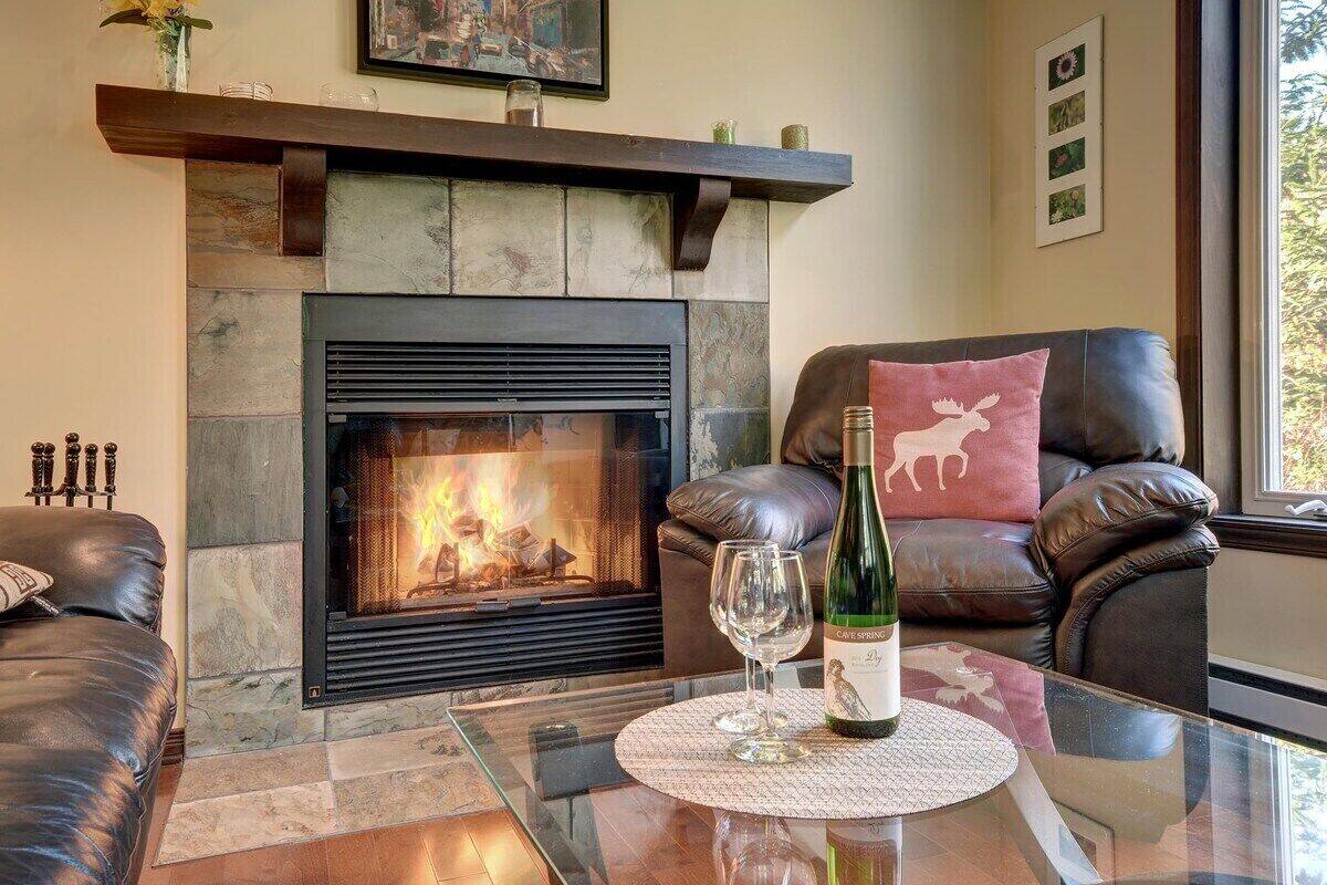 Ein Wohnzimmer mit Kamin aus Stein, einer Ledersofa und einem Glastisch mit einer Weinflasche und einem Glas.