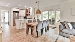 A modern kitchen with a central island, dining area with chairs, and a sofa. - L'Aiglon - RVMT (Mont-Tremblant)