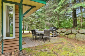 An outdoor patio with a table and chairs, a grill, and a stone wall.