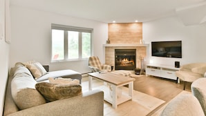 A modern living room with a fireplace, a flat-screen TV, and a comfortable seating area. - L'Aiglon - RVMT (Mont-Tremblant)