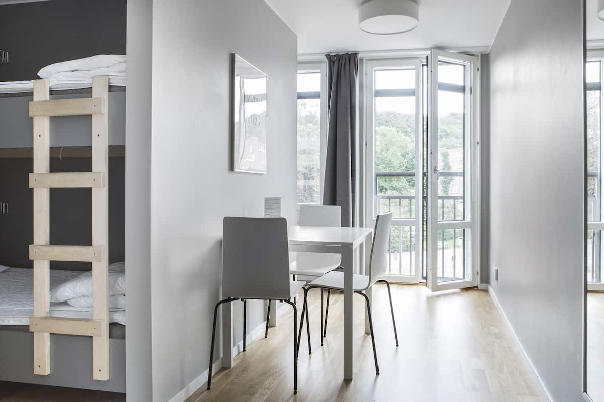 Ein moderner, gut beleuchteter Raum mit einem Etagenbett, einem Esstisch mit Stühlen und großen Fenstern mit Blick auf Grünflächen.