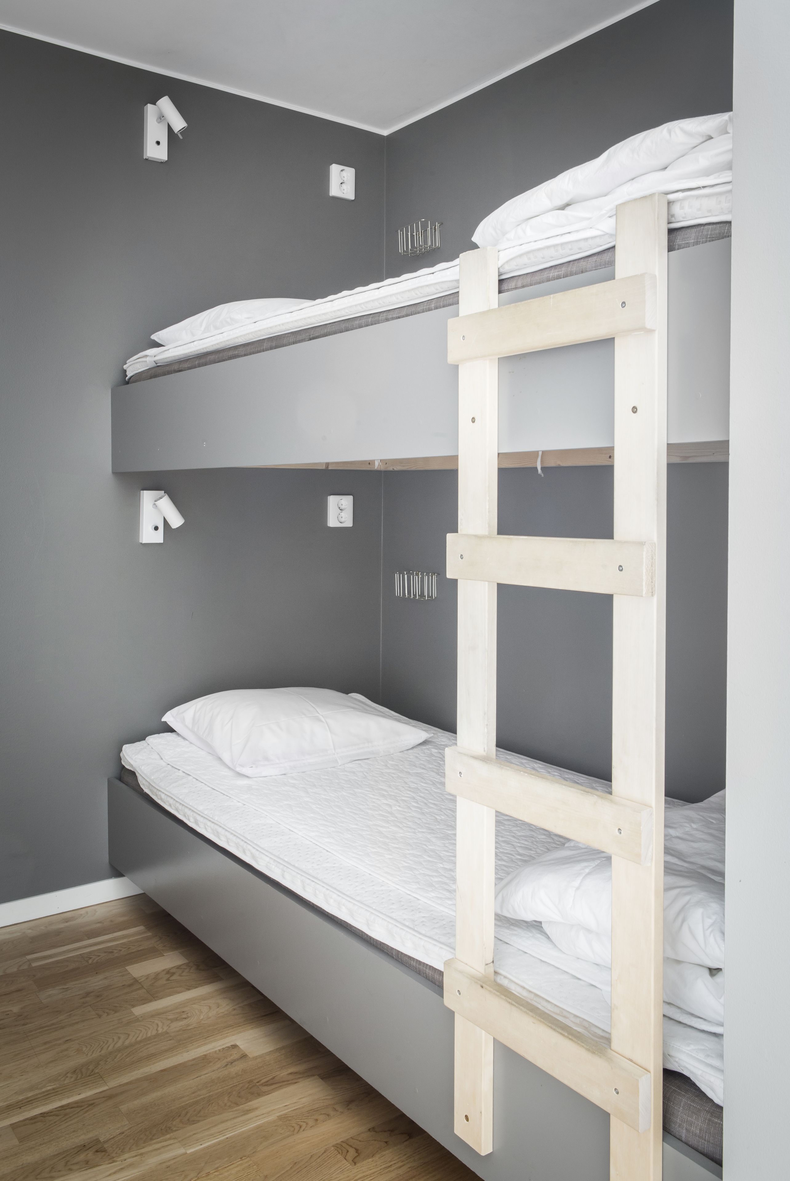 Una cama litera con escalera de madera, paredes grises y suelo de madera.