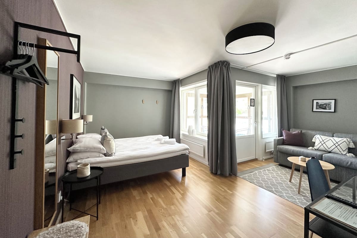 Ein modernes Hotelzimmer mit Bett, einer Couch, einem Esstisch und einem großen Fenster mit Vorhängen.