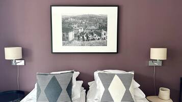 Une chambre d’hôtel avec un lit, deux oreillers, une photographie en noir et blanc encadrée accrochée au mur, et deux lampes de chevet.